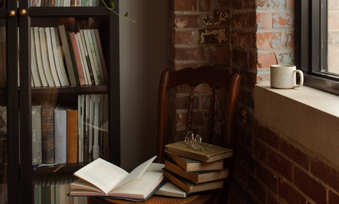 A chair with multiple books stacked near it near a bookshelf