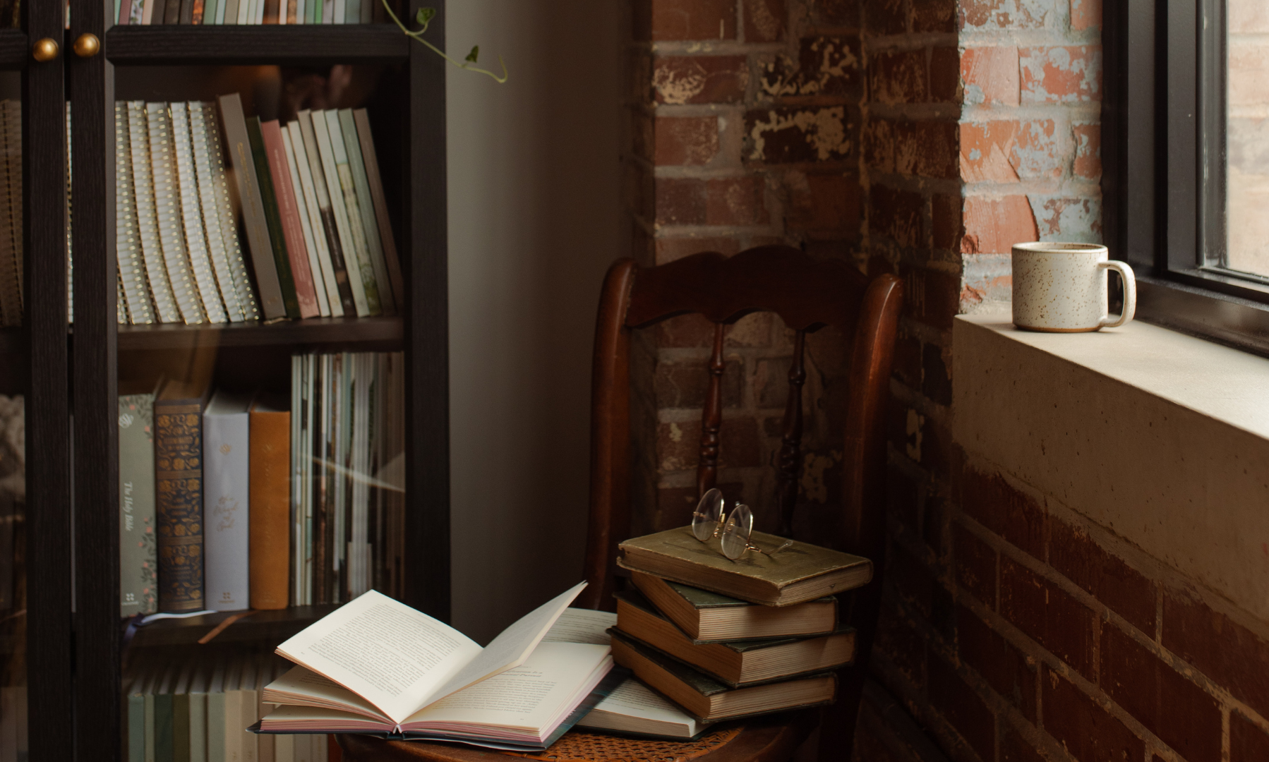 A chair with multiple books stacked near it near a bookshelf