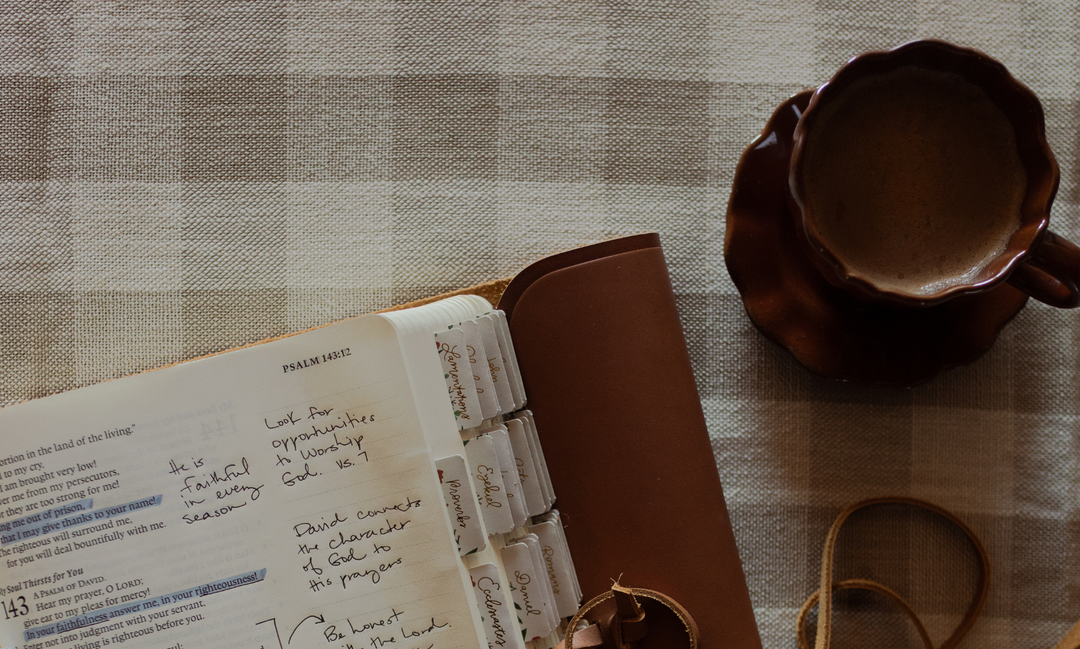 An open bible next to a cup of coffee on a cross woven blanket