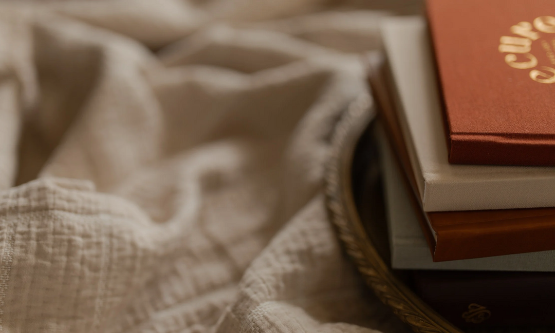 Multiple hardcover books on a gold tray on a cream colored blanket