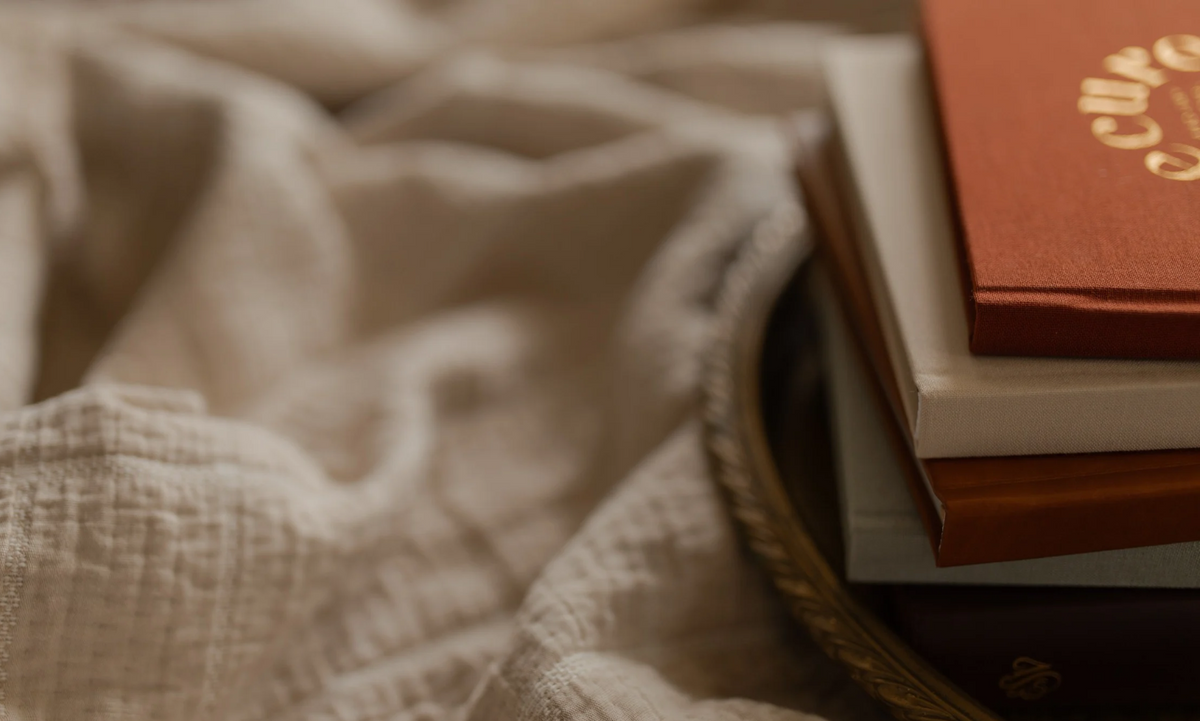 Multiple hardcover books on a gold tray on a cream colored blanket