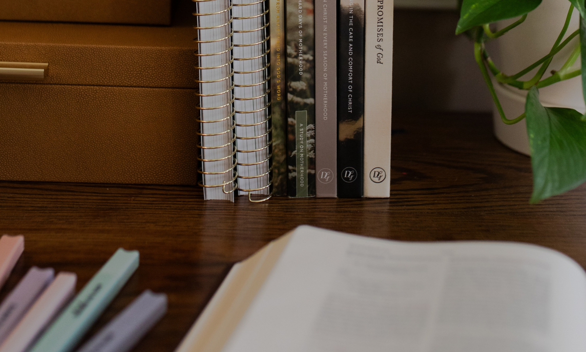 Multiple books standing up on a wooden table with an open book in front of it