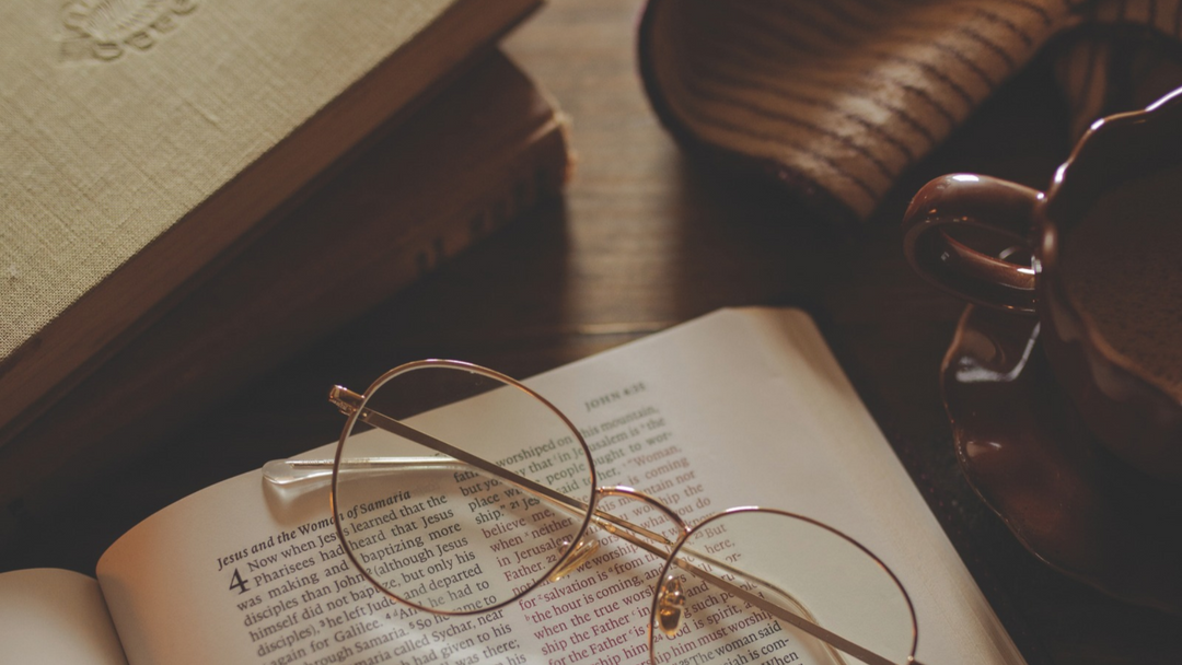 A pair of glasses on a open bible near a wooden table
