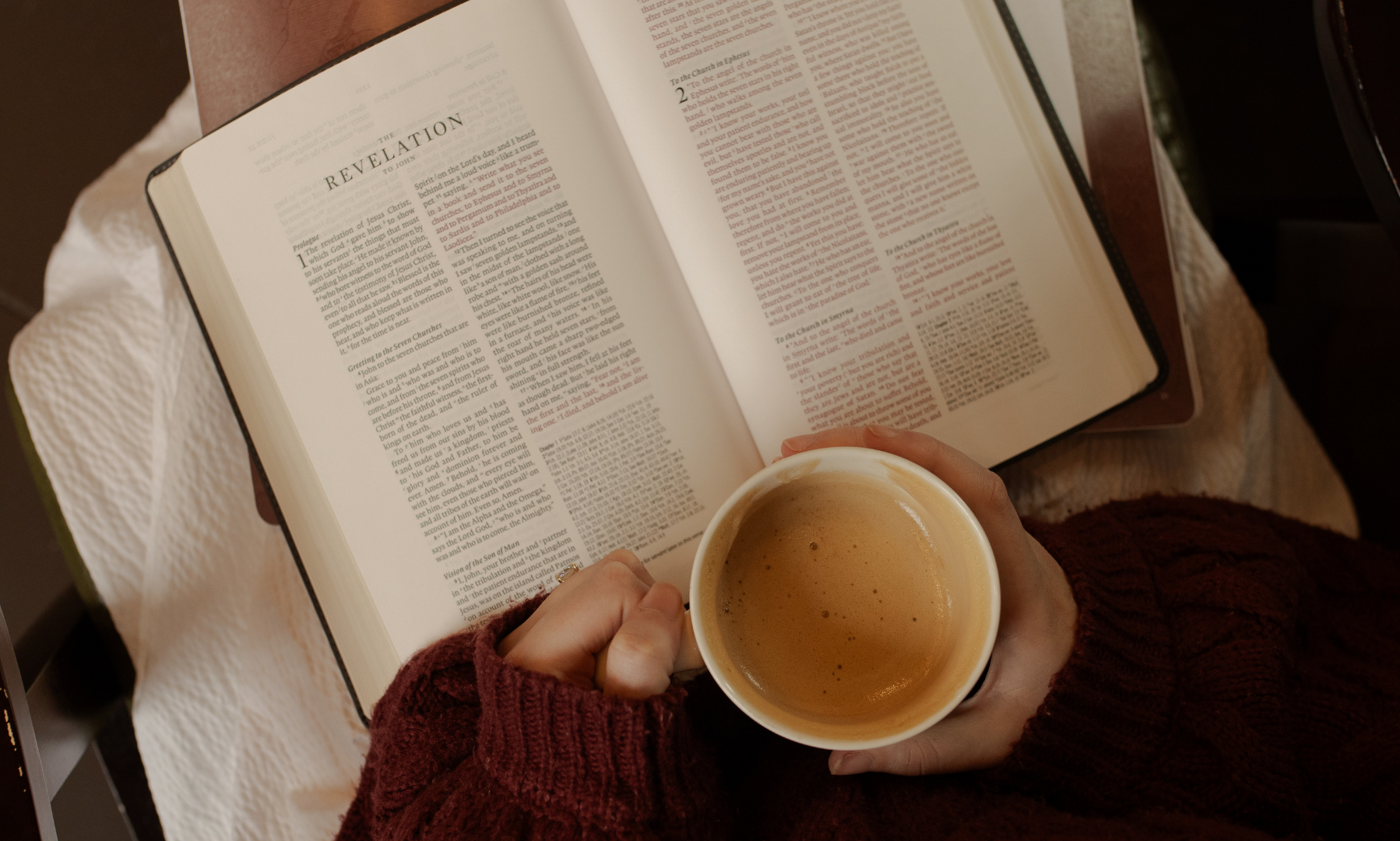 A woman holding a cup of coffee while reading the bible