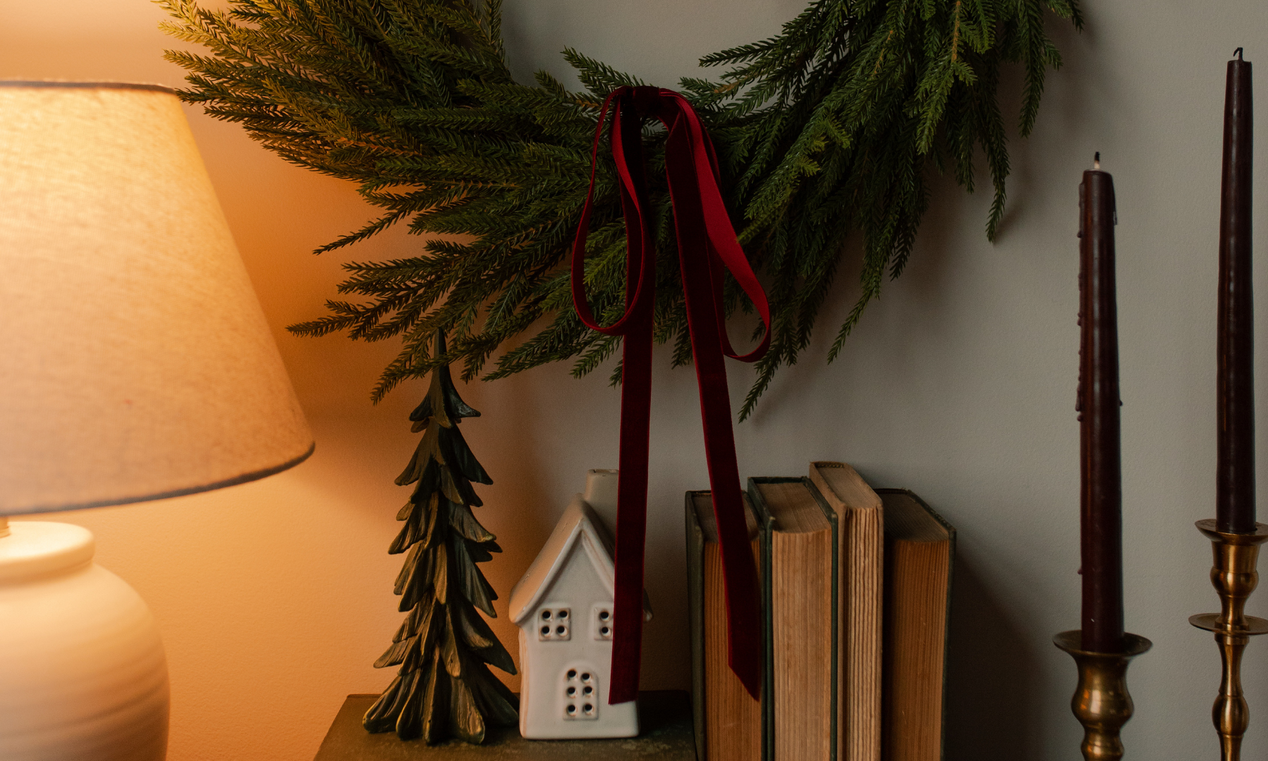 Greenery hanging on a wall with red ribbon near some books and candles