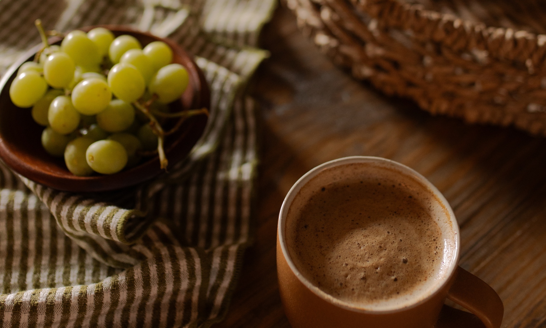 A bowl of green grapes on a towel next to a brown coffee cup