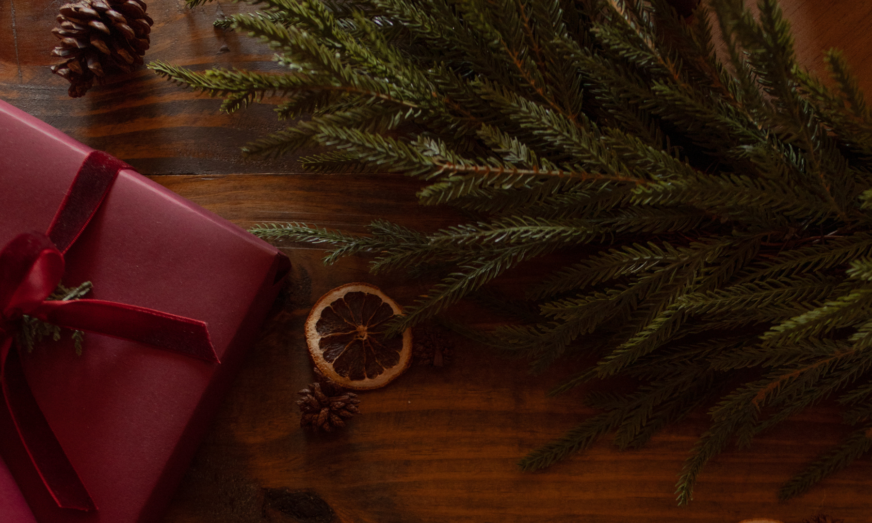 A Green branch, a dried orange slice, and a red wrapped gift on a wooden table