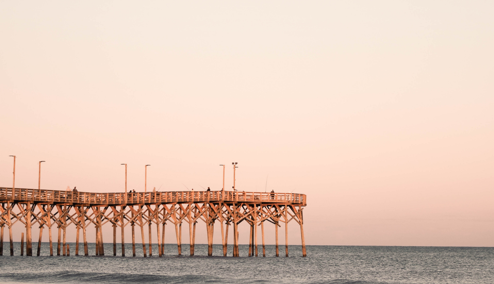 A pier over a clear blue ocean with a pink and clear sky
