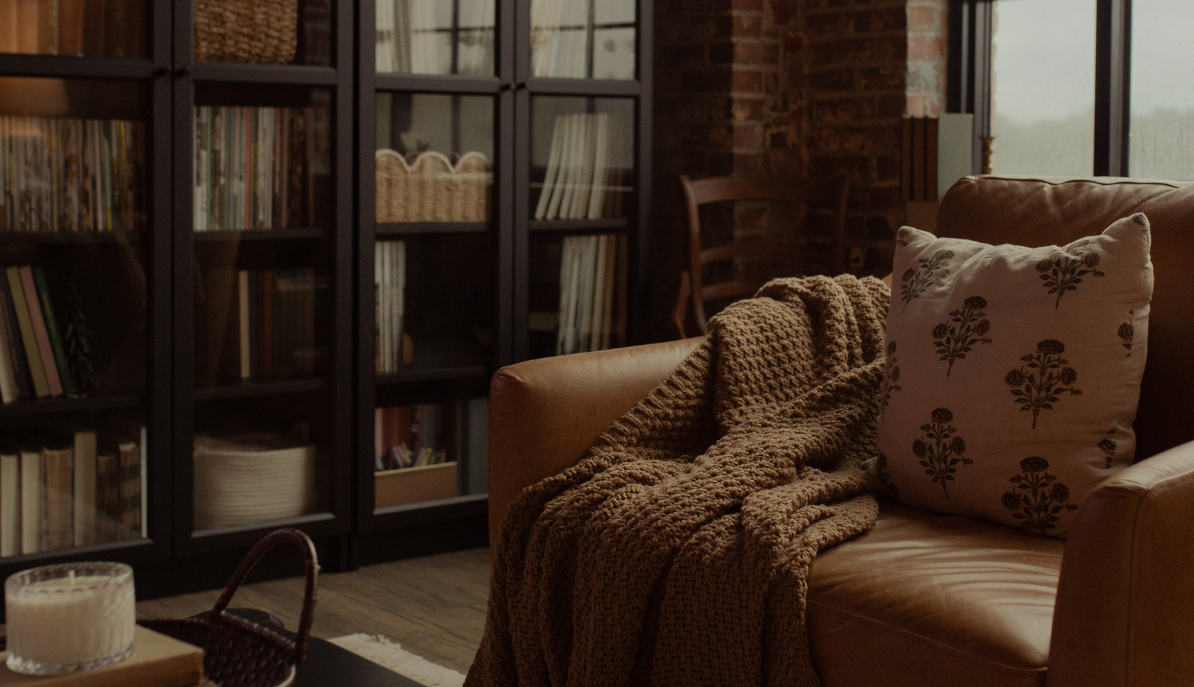 A brown leather couch and a brown blanket next to a black framed bookcase