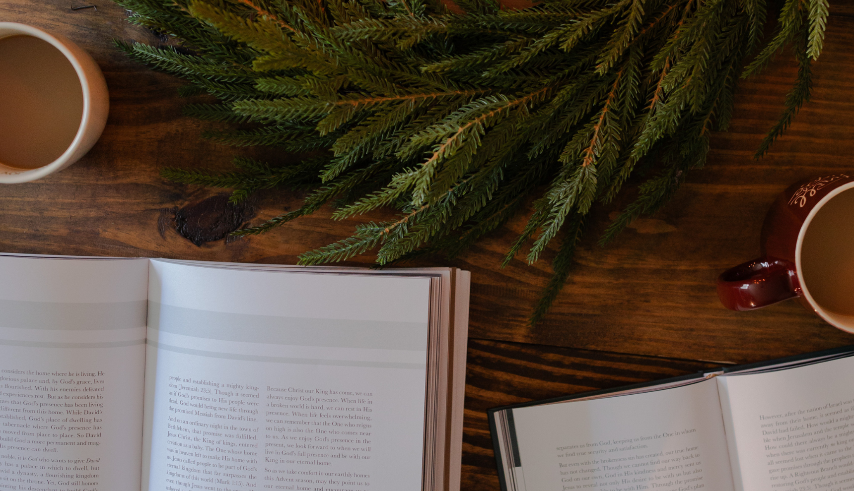 An open bible study on a wooden desk near some green garland