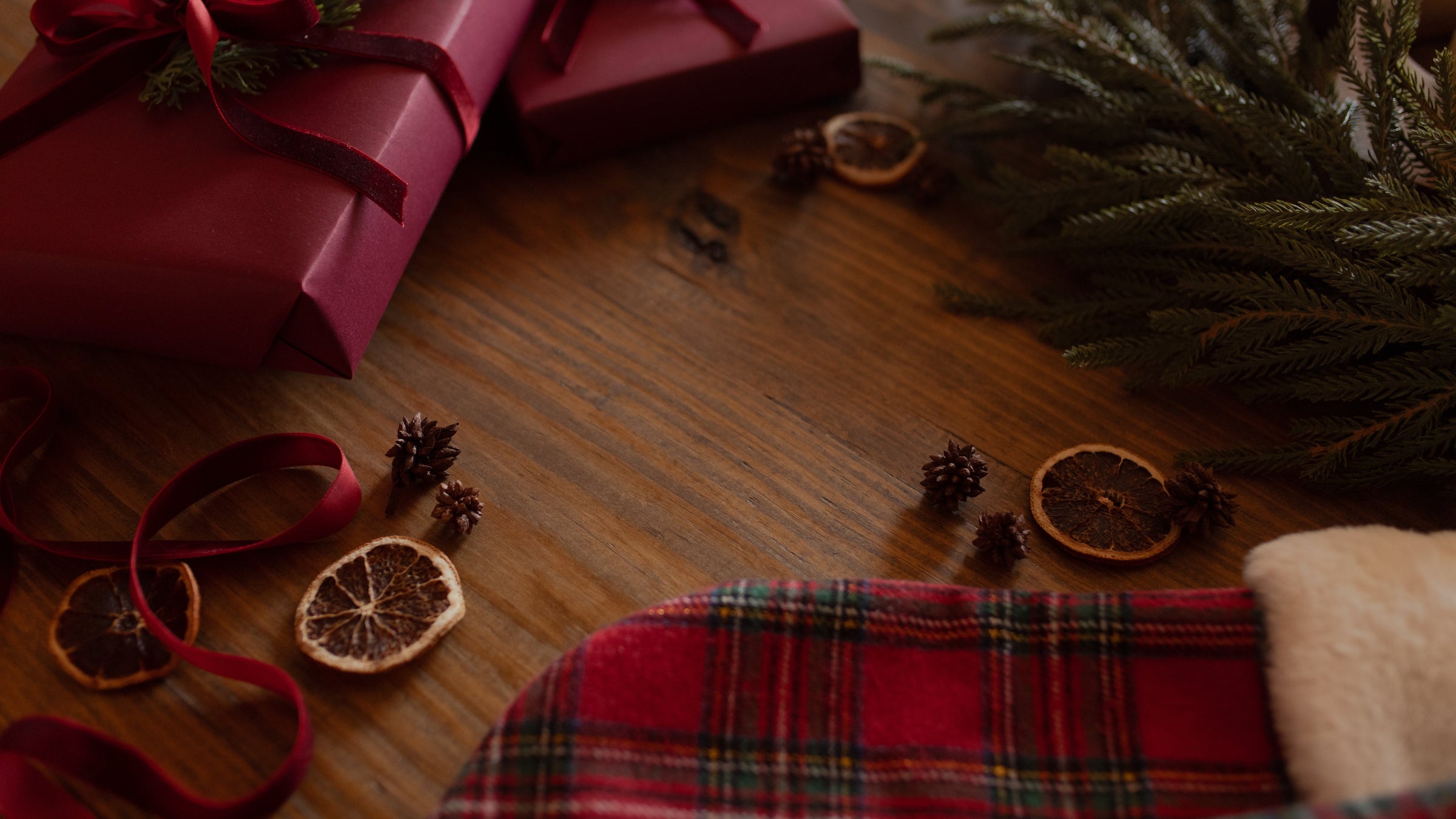 Orange slices on a wooden table near some garland and some red wrapped gifts