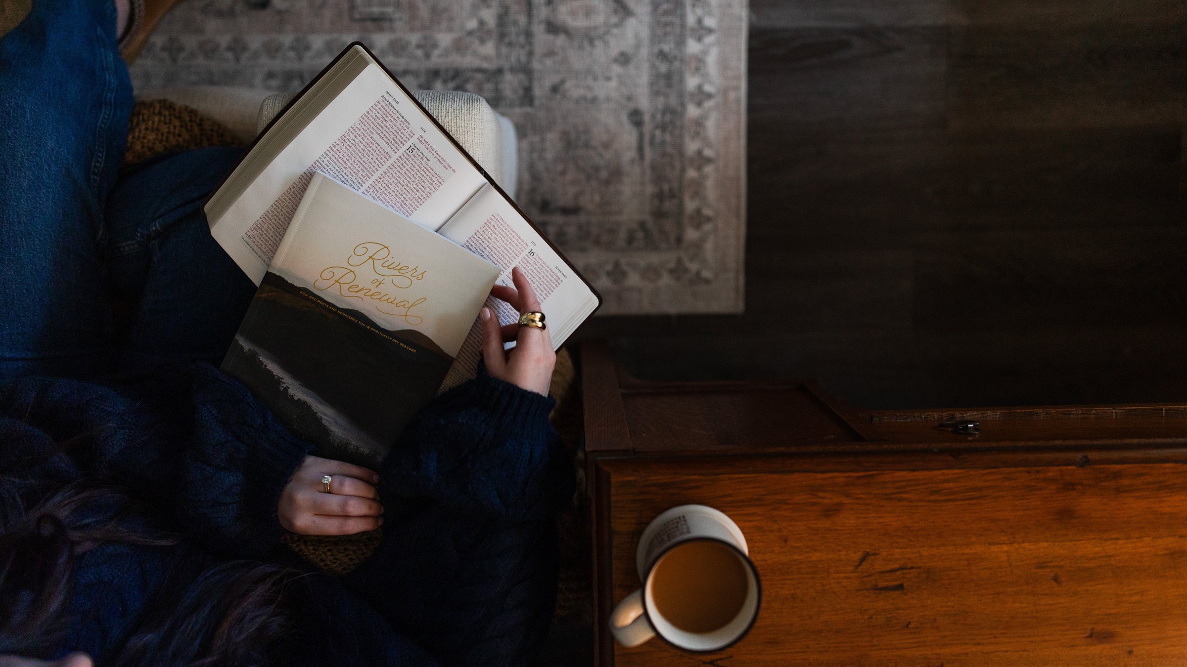 Woman holding a Rivers of Renewal Study on an open bible next to a coffee cup on a wooden table