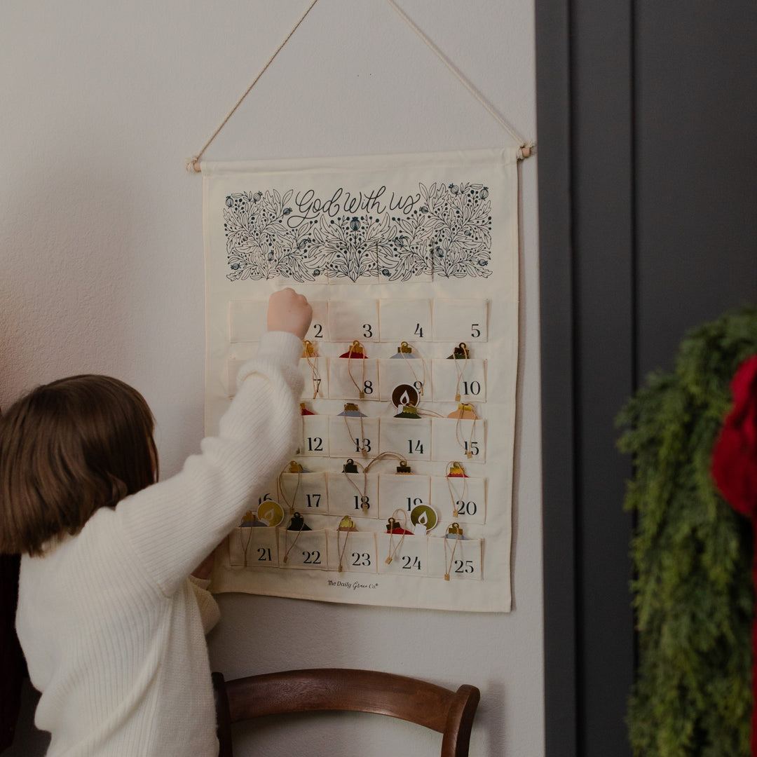 A child interacting with a Christmas countdown calendar on a wall, next to a chair.