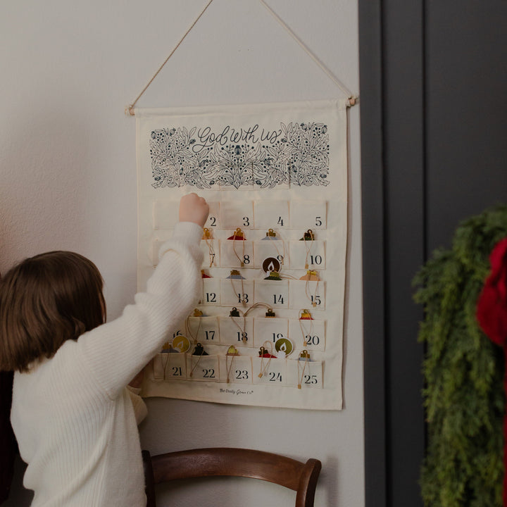 A child interacting with a Christmas countdown calendar on a wall, next to a chair.