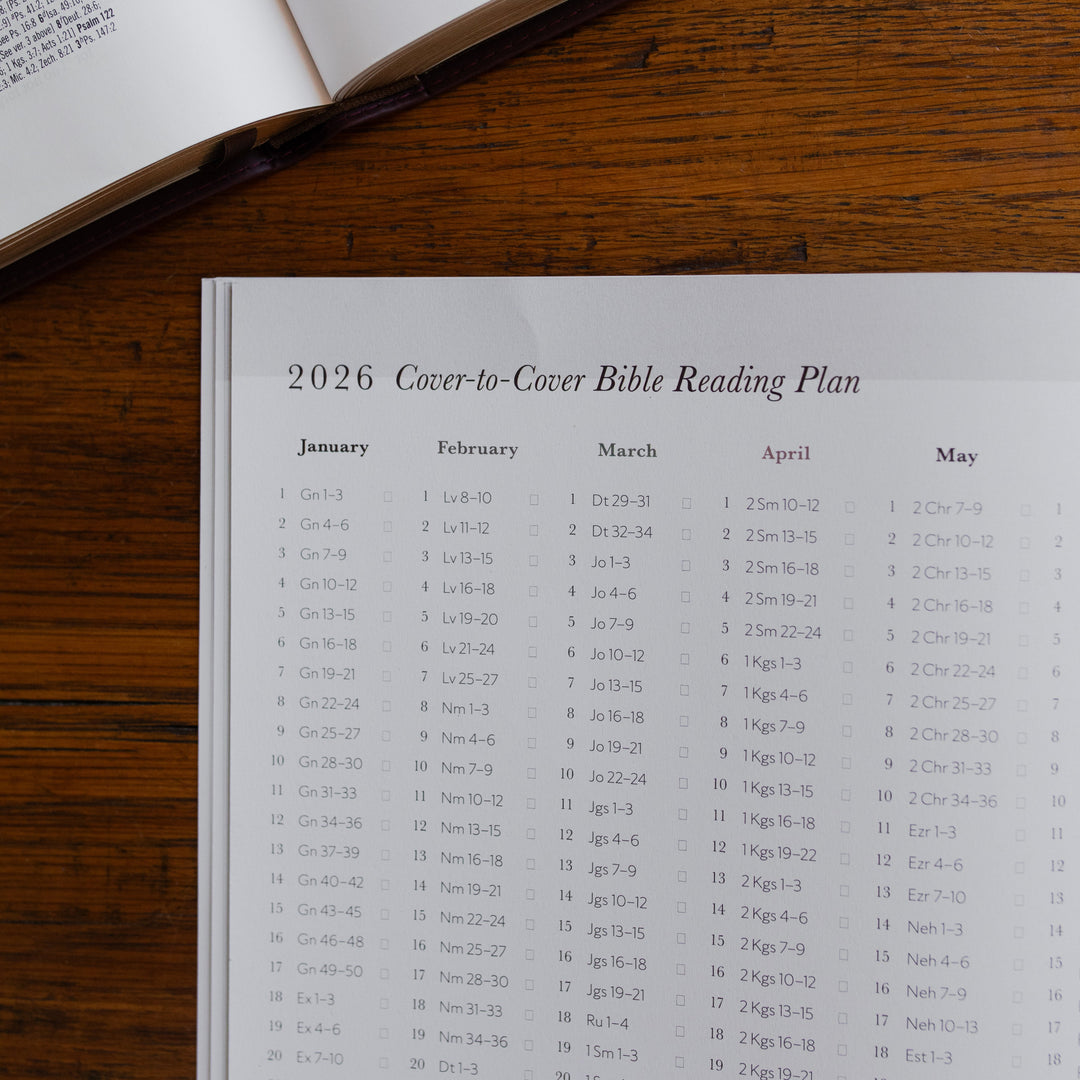 Up close of the 2026 Prayer Calendar opened to the 2026 Reading Plan page on a wooden table next to an open bible