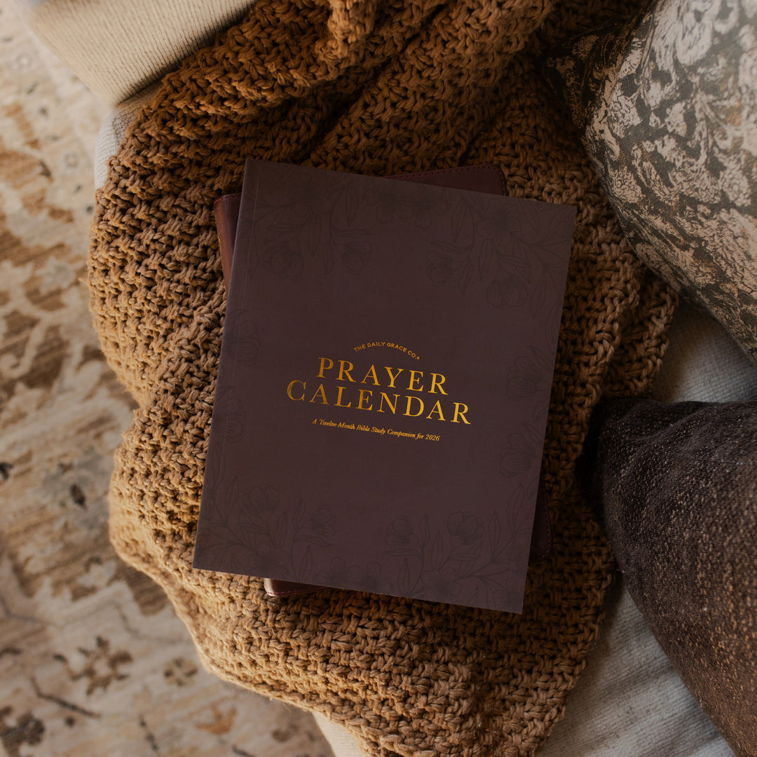 2026 Prayer Calendar on a closed journal on a brown woven blanket on a cream colored couch