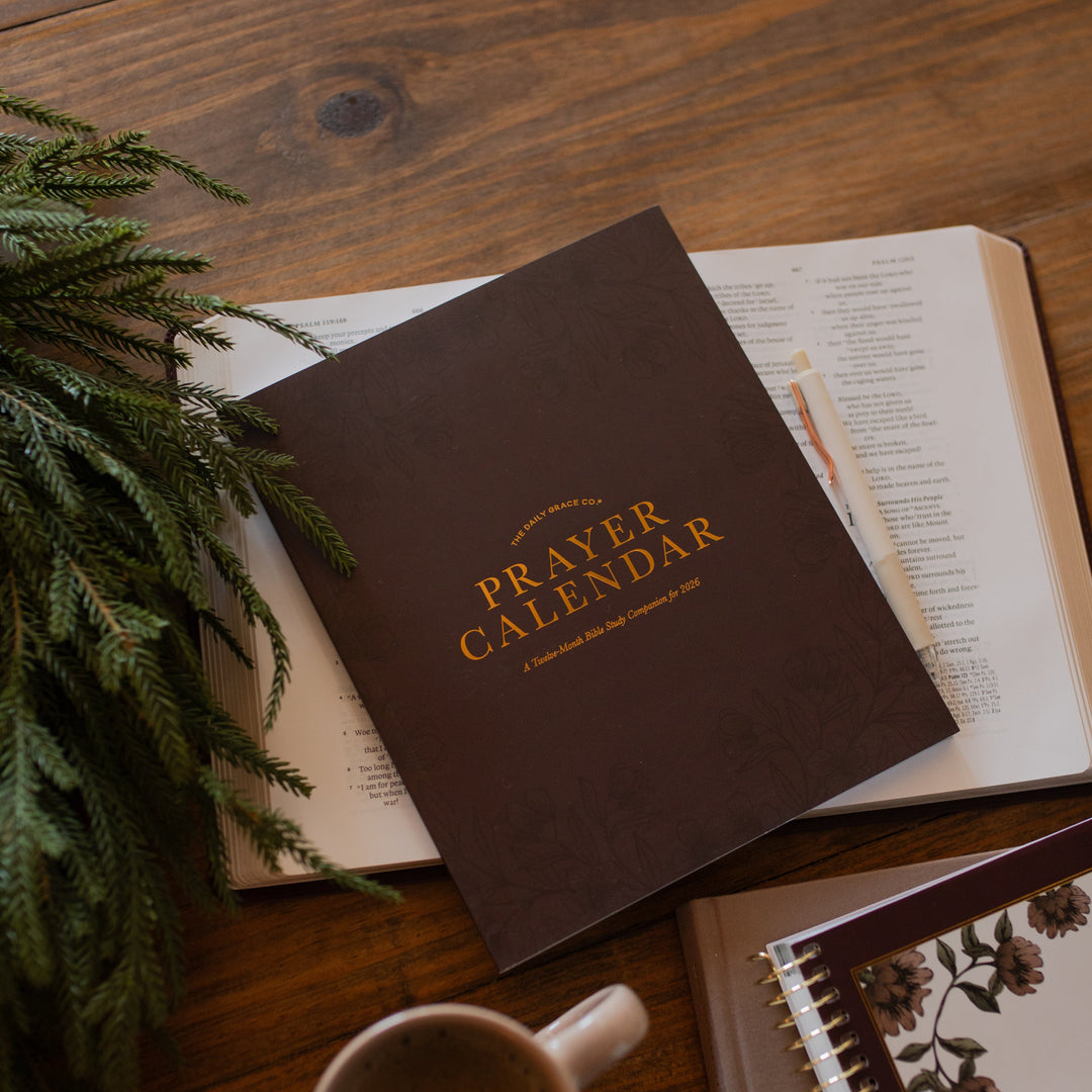 2026 Prayer Calendar on an open bible on a wooden table next to a coffee cup