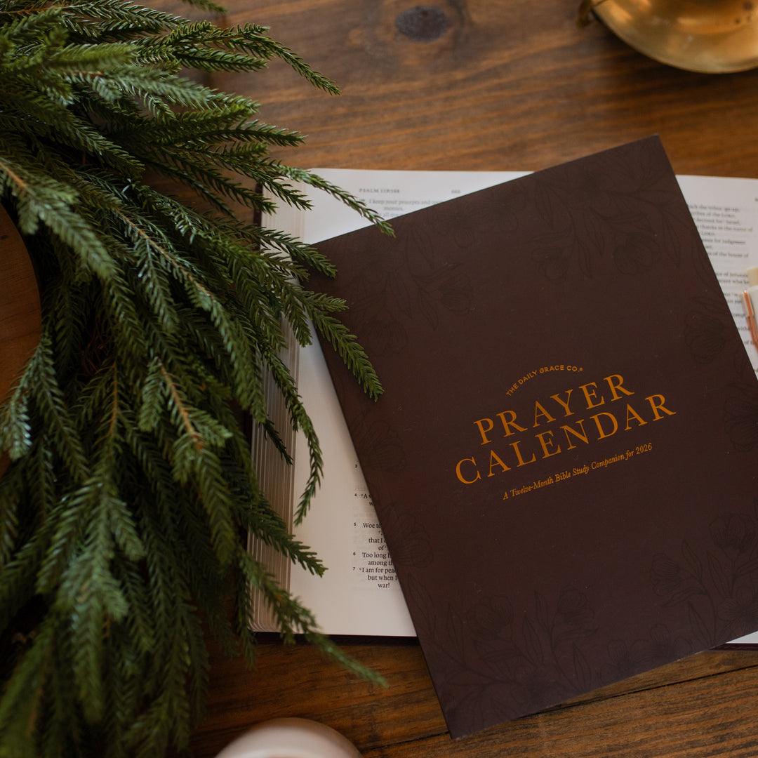 2026 Prayer Calendar on an open bible on a wooden table next to some greenery
