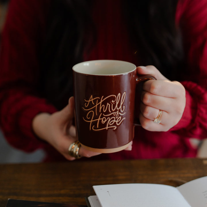 A woman holding the Thrill of Hope Mug towards the camera