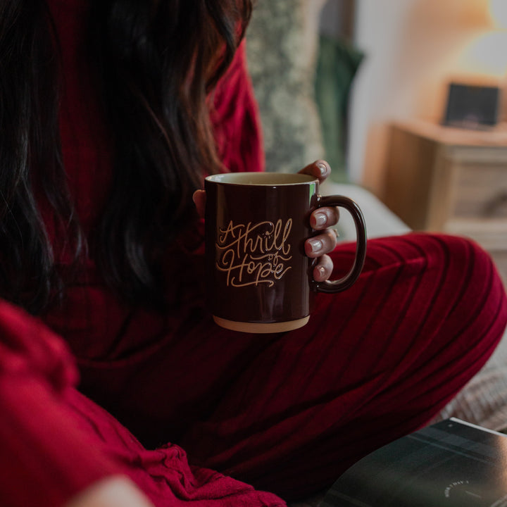 A woman that is sitting is holding a Thrill of hope mug 