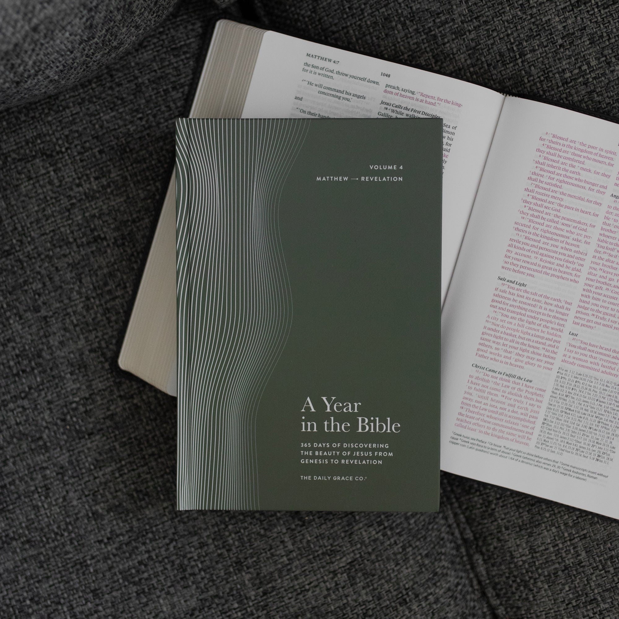 A Year in the Bible Vol 4 Hardcover cover on an open bible on a grey couch cushion