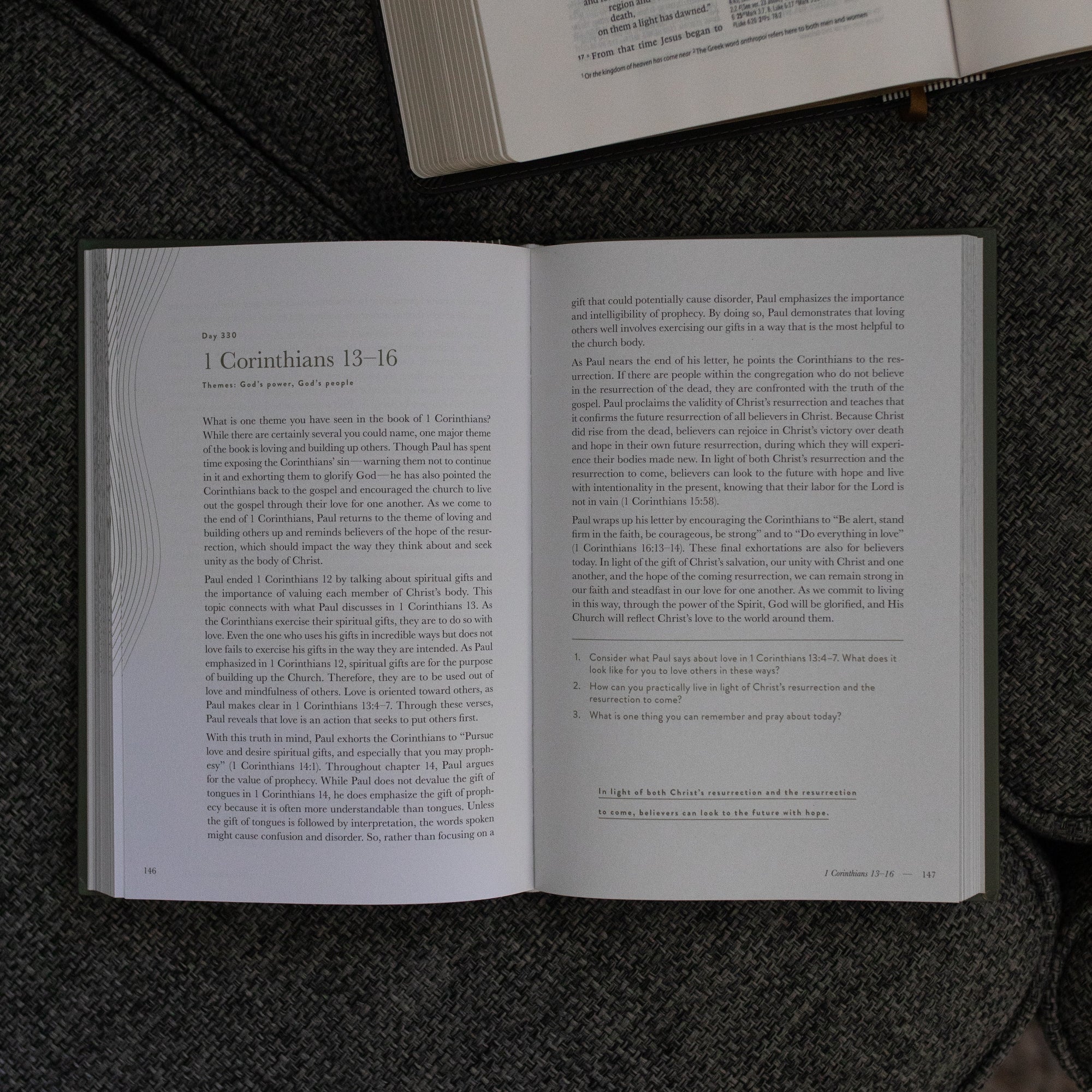 A Year in the Bible Vol 4 Hardcover opened to the Corinthians reading page near an open bible on a grey couch cushion