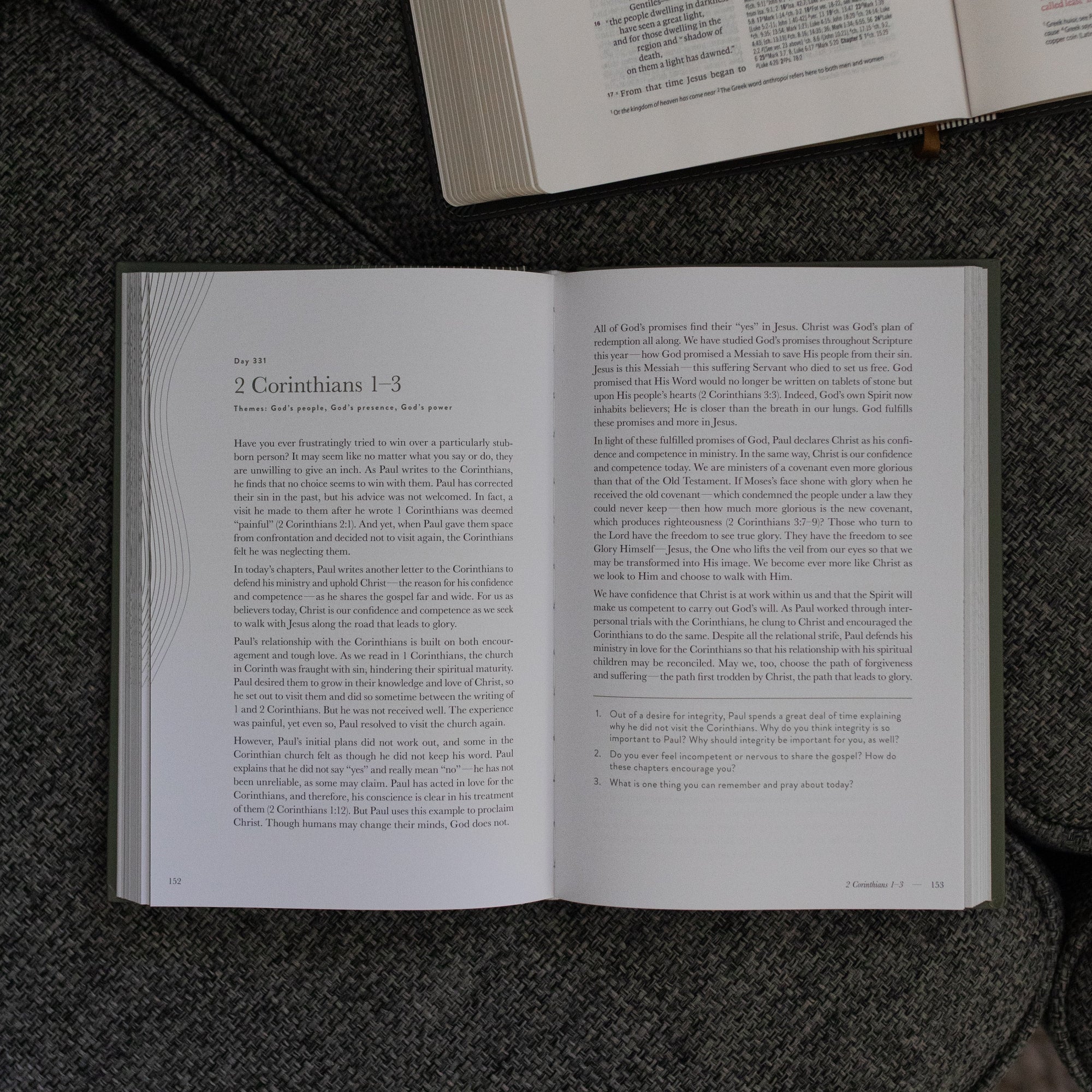 A Year in the Bible Vol 4 Hardcover opened to the 2nd Corinthians reading page near an open bible on a grey couch cushion