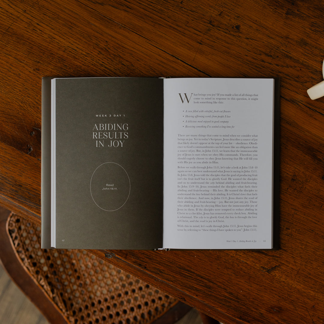 The Abide Hardcover opened to the Week 3 Day 1 Scripture reading page on a wooden table