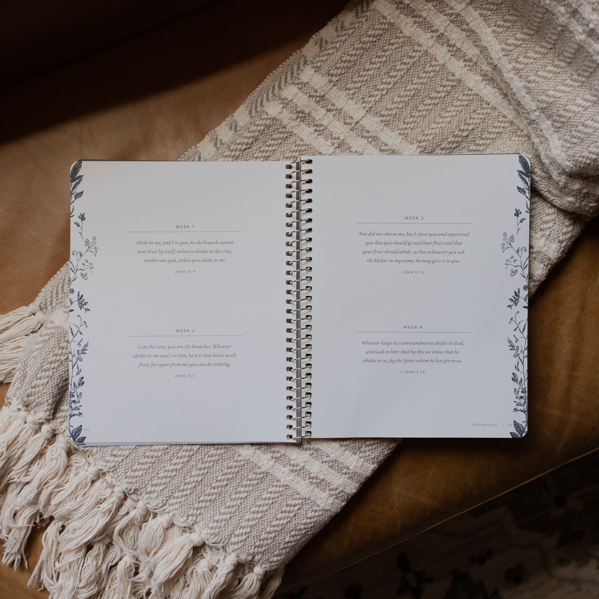 The Abide Spiral opened to the Weekly scripture reading page on a cream colored blanket