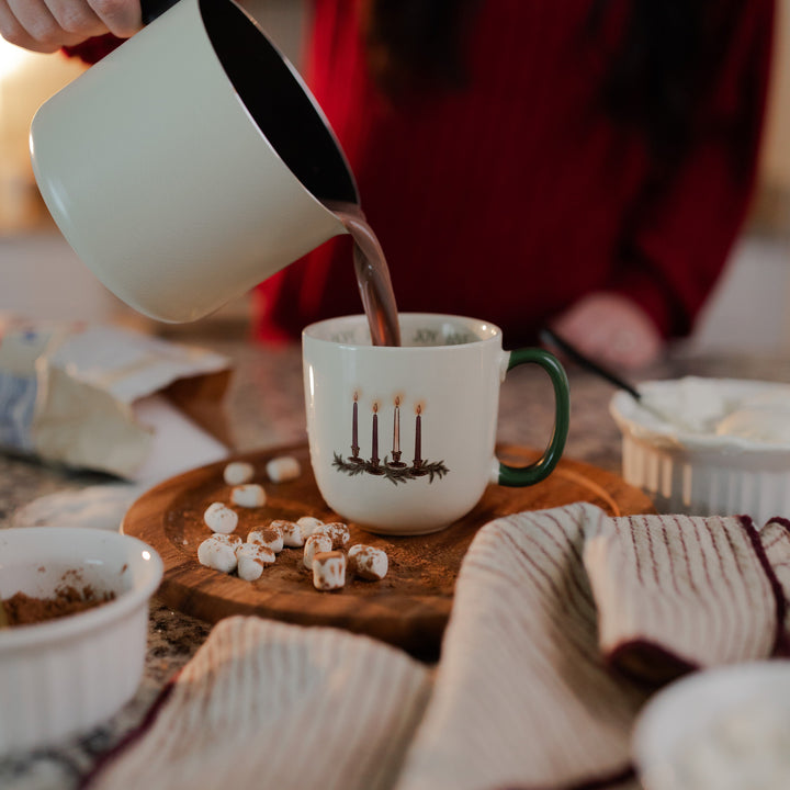A woman pouring hot chocolate into the Advent Adventure Mug sitting on a wooden table