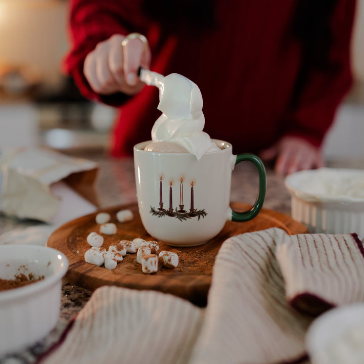 A woman pouring whipped cream into the Advent Adventure Mug sitting on a wooden table