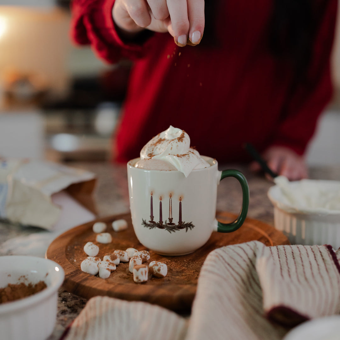 A woman sprinkling cinnamon onto the Advent Adventure Mug sitting on a wooden table