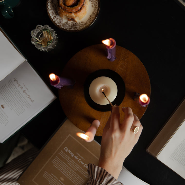 A woman lighting the middle candle on a dark wooden table