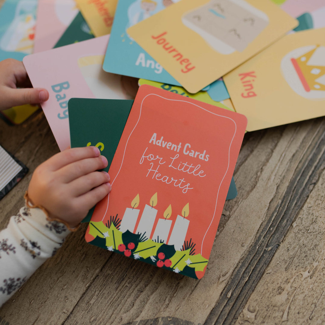 Colorful Advent Cards for Little Hearts on a wooden surface with a child's hand reaching for one.