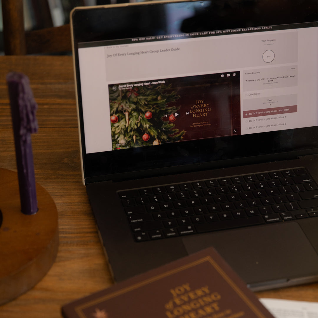 A laptop on a wooden table displaying a website template or digital guide, with a purple candle in a wooden holder on the left and a brown book in the foreground.