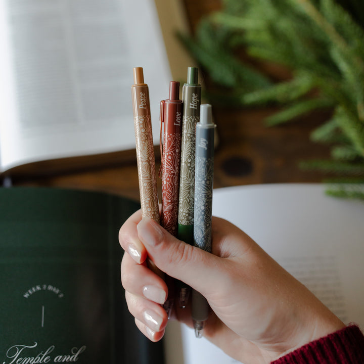 A woman holding all 4 of the advent pens from the advent pen set over a bible study