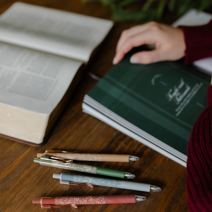 A womans hand resting on an open bible study next to all four of the pens from the advent pen set