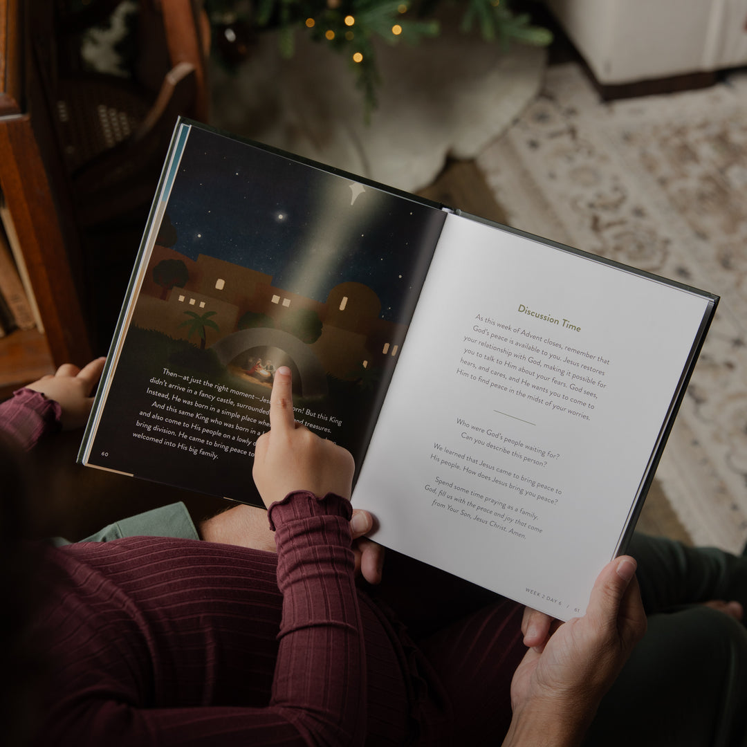 A person holding an open children's book in a cozy indoor setting, pointing at a starry night scene on one page while reading text on the other page.