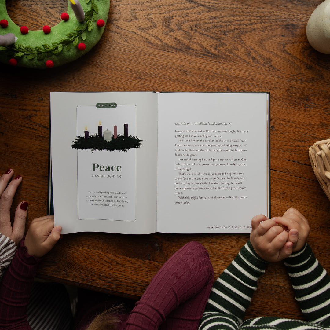An open children's book titled 'Peace' is laid on a wooden table, viewed from above. Two children's hands and arms in striped sweaters are visible holding the book open.