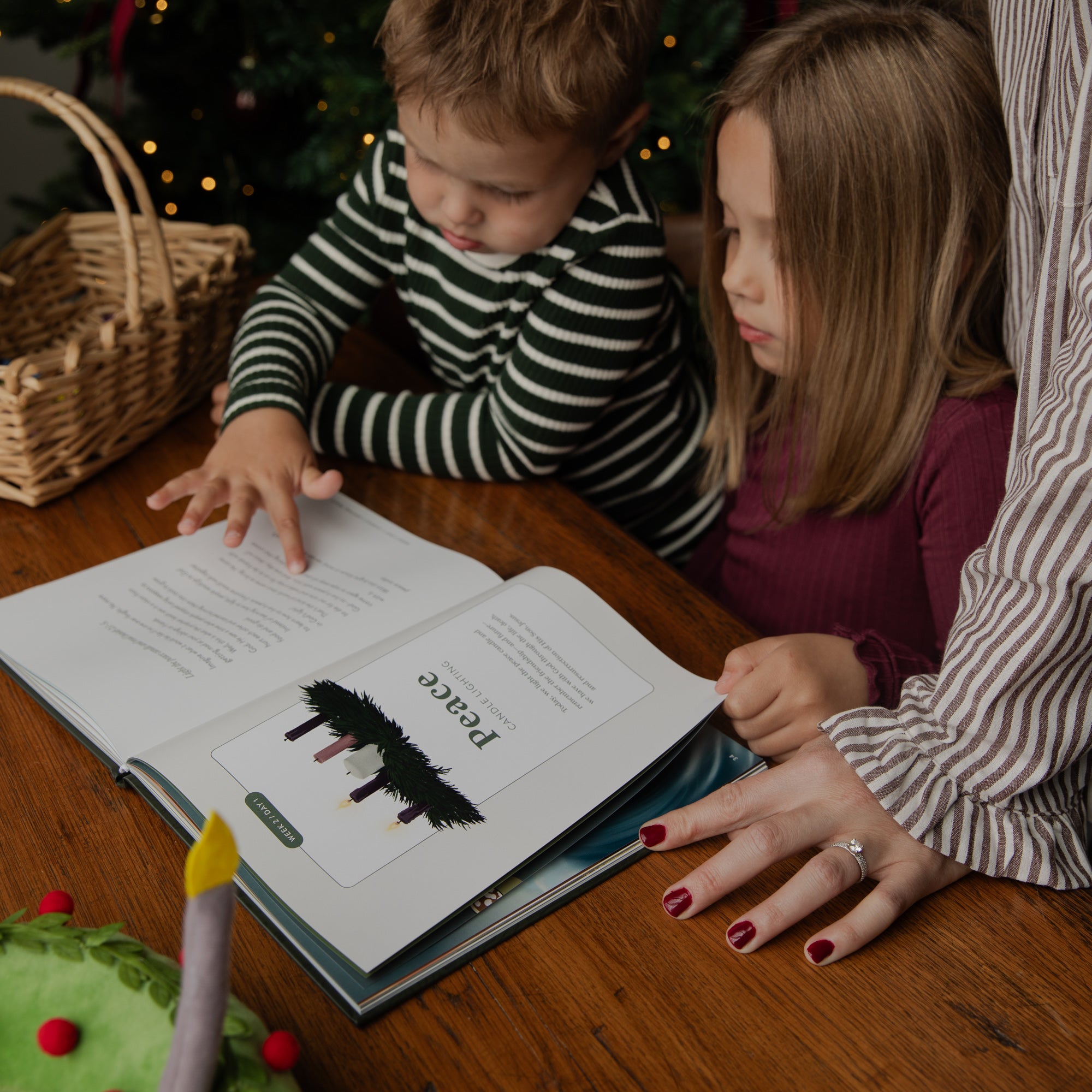 A child and a woman are gathered around a wooden table, reading a book together. The child wears a black and white striped long-sleeve shirt, and the woman wears a brown and white striped blouse.