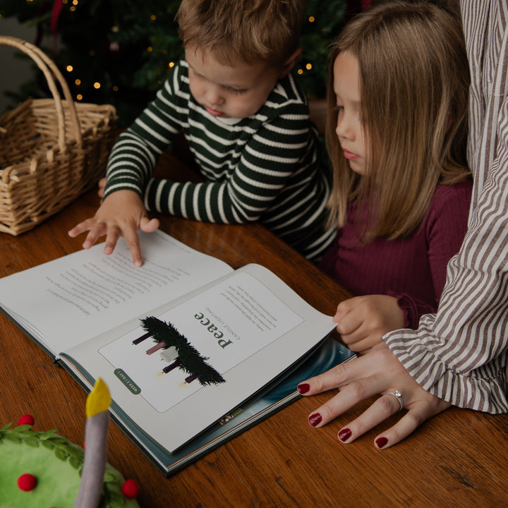 A child and a woman are gathered around a wooden table, reading a book together. The child wears a black and white striped long-sleeve shirt, and the woman wears a brown and white striped blouse.