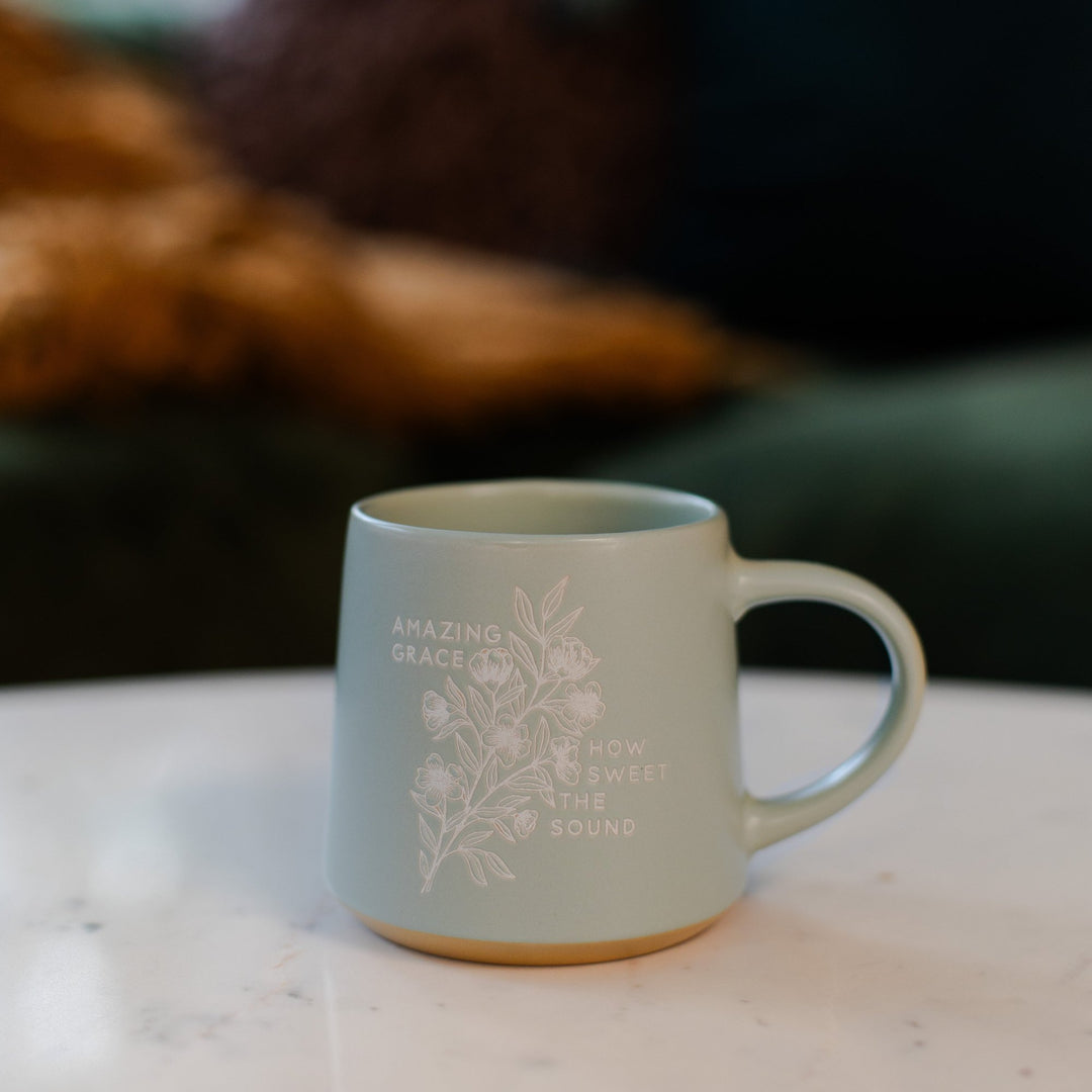 Coffee Mug with floral designs that says amazing grace how sweet the sound sitting on a marble table 