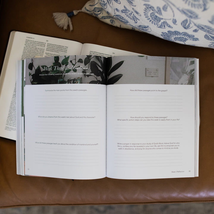 Amen from Eden to Eternity Matte Study opened to Week 3 Reflections page laying on an open bible on a brown leather couch next to a white and blue decorated pillow