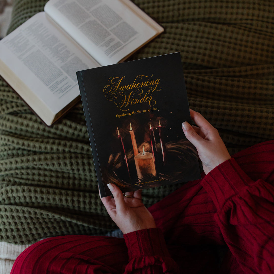 A woman's hand holding the Awakening Wonder Study cover over a green woven blanket near a open bible