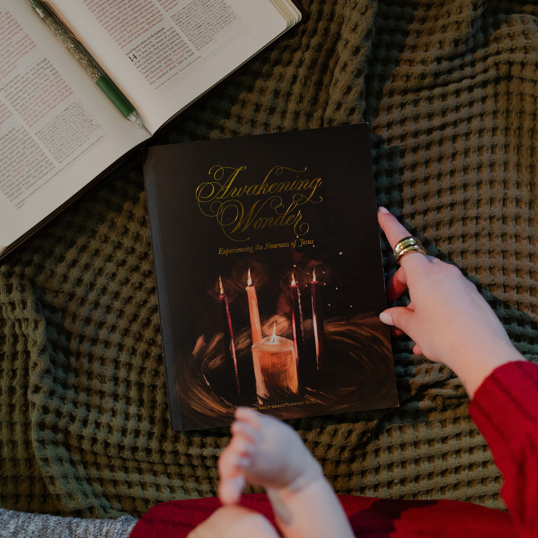 A woman touching the edge of the Awakening wonder study cover with a baby sitting on their lap and next to an open bible