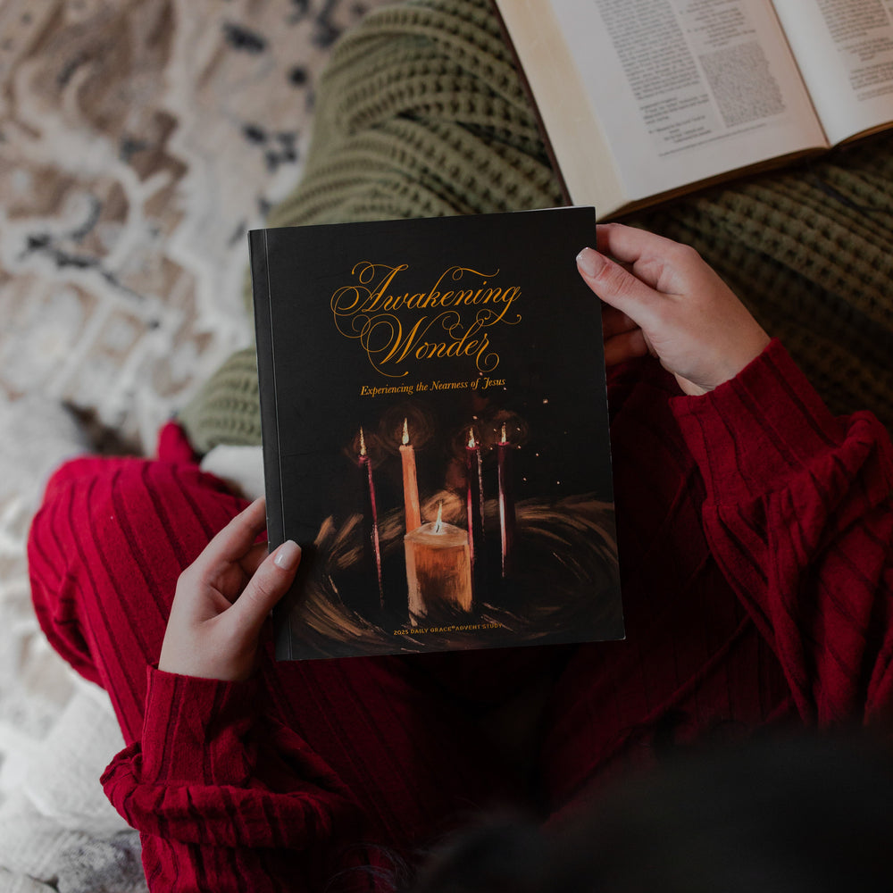 A woman holding the Awakening Wonder Study cover over a green woven blanket near a open bible