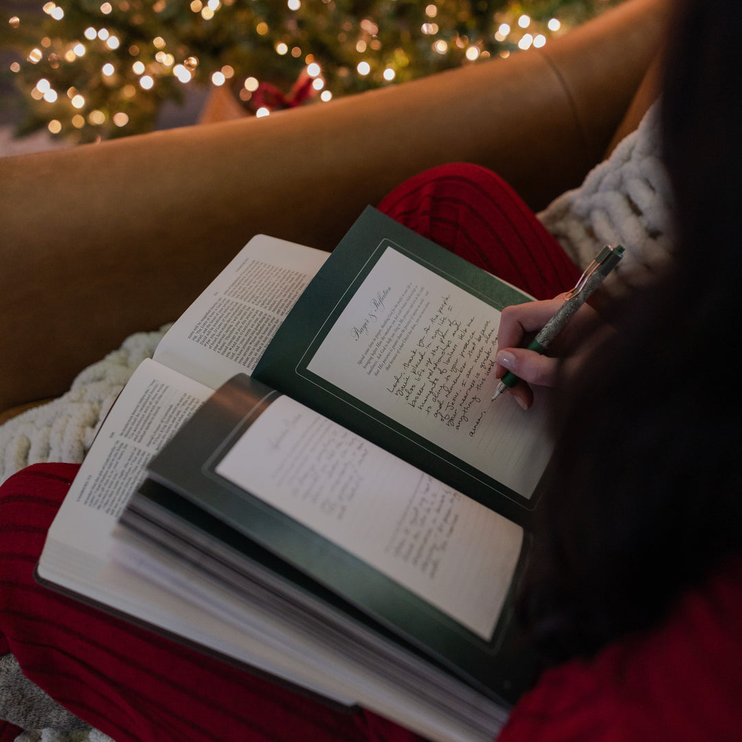 A woman writing in the Awakening Wonder Study while sitting on a leather couch