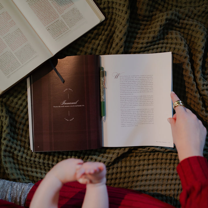 A woman holding the Awakening Wonder study open by the edge with a pen resting in the middle of the study next to an open bible
