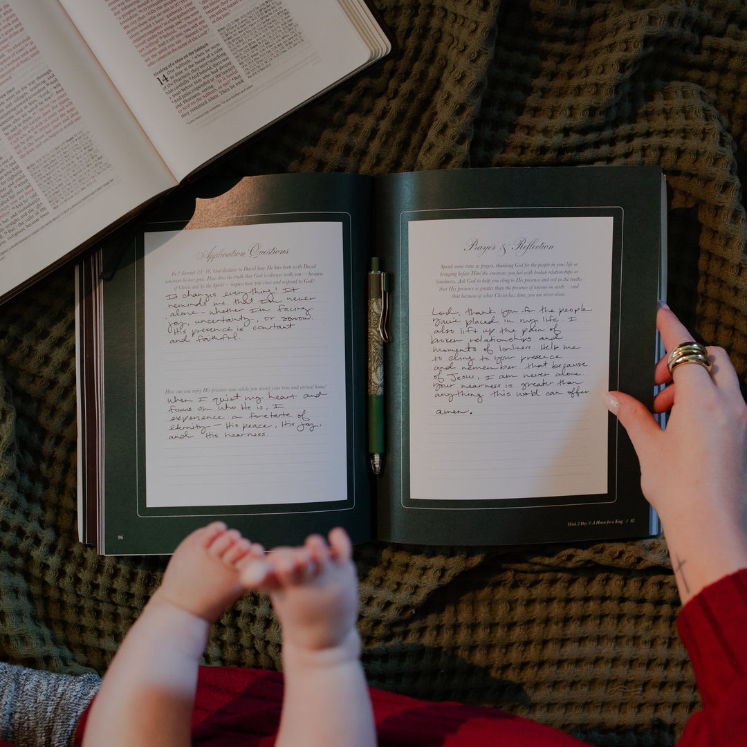 A woman holding open the Awakening Wonder study to the question and reflection page while a baby is sitting on their lap next to an open bible