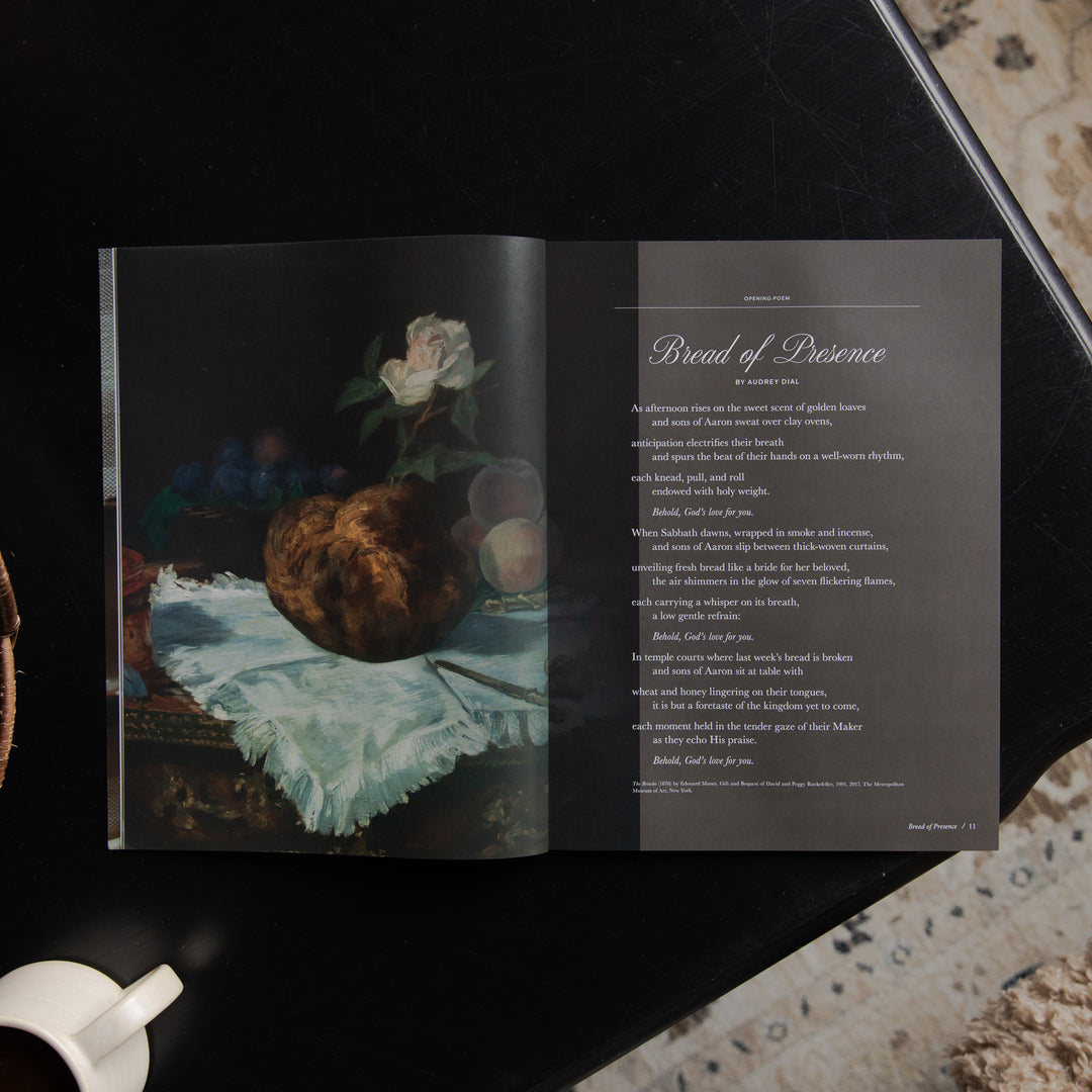 An open printed book or magazine laid on a dark surface, showing a still life painting on the left page and a poem titled 'Bread of Presence' on the right page.